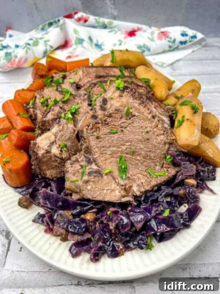 A hearty serving of slow cooker German Pot Roast with tender beef, red cabbage, and baby potatoes on a white plate, ready to be enjoyed.