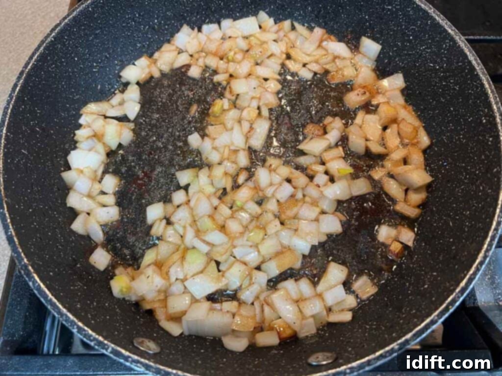 Chopped onions and garlic sautéing in the reserved bacon fat in a frying pan, becoming tender and fragrant.