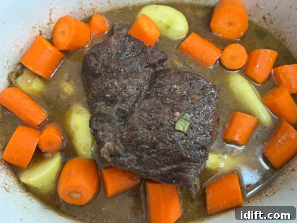 Baby potatoes and carrots being added to the slow cooker with the beef and broth, halfway through the cooking.
