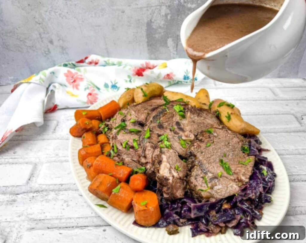 A plate of German Pot Roast with gravy being poured over the sliced beef, red cabbage, and potatoes.