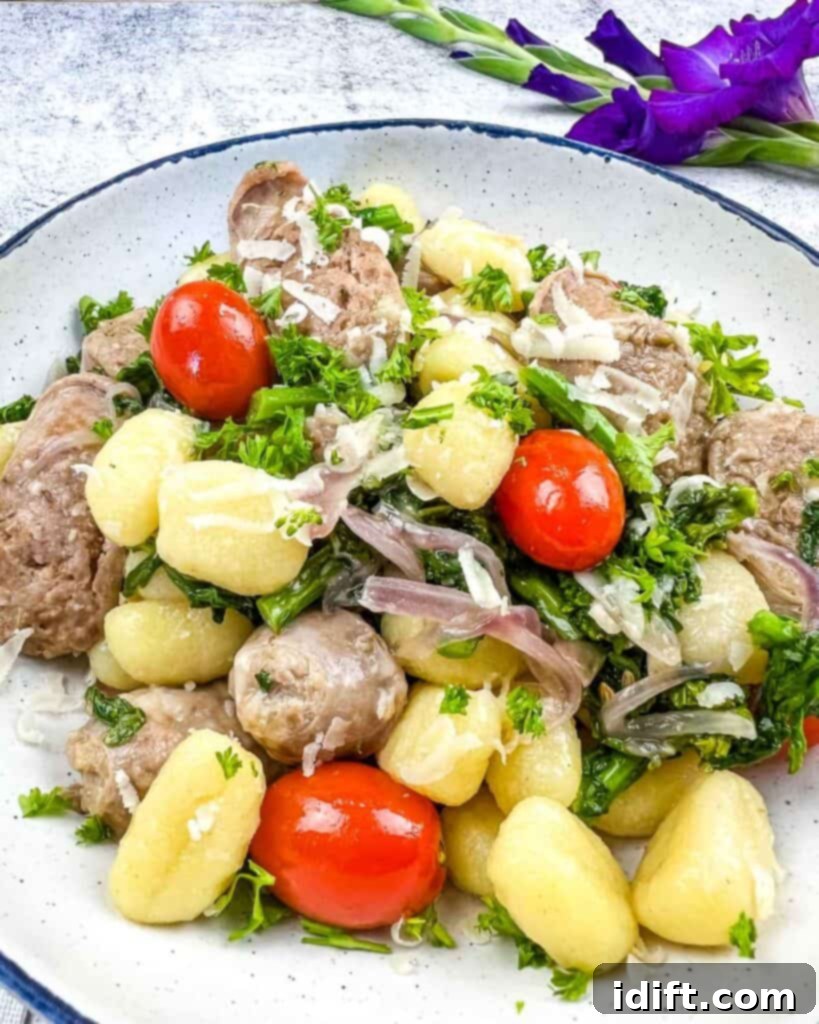 A vibrant skillet gnocchi dish with sausage, broccoli rabe, and cherry tomatoes, garnished with Parmesan cheese, served on a white plate.