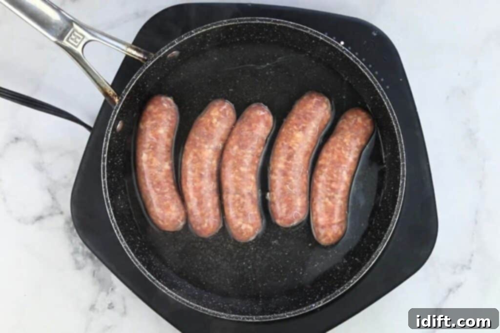 Italian sausages simmering in a shallow pan of water, par-cooking before slicing.