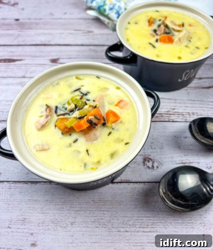 Rich Chicken and Wild Rice Soup 2 Two bowls of Creamy Chicken & Wild Rice Soup on a wooden table.