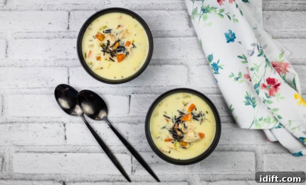 Rich Chicken and Wild Rice Soup 10 Two bowls of creamy chicken and wild rice soup with spoons on a white brick wall background.