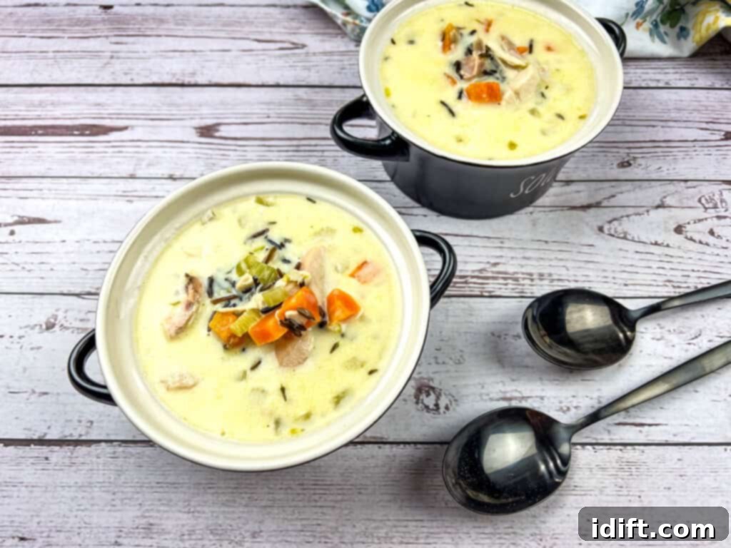 Rich Chicken and Wild Rice Soup 3 Two bowls of Creamy Chicken & Wild Rice Soup on a wooden table.