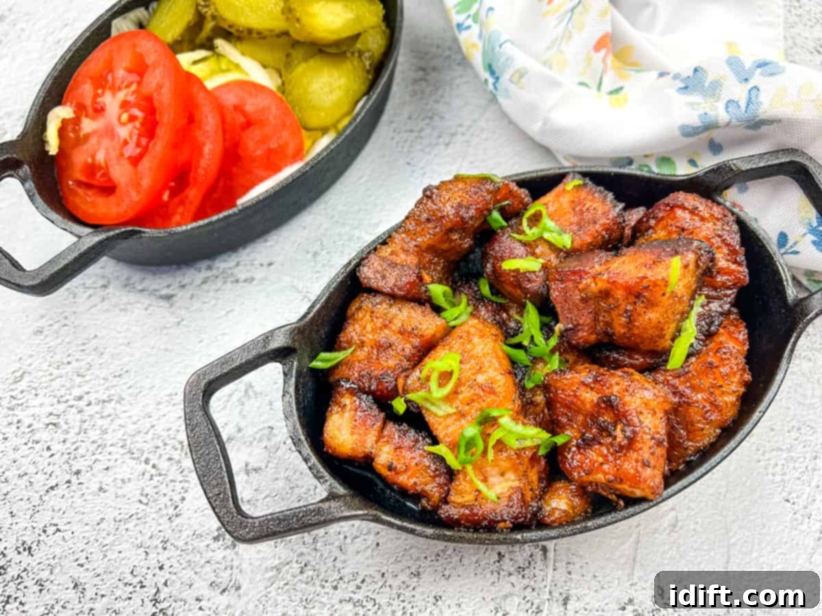 A plate of smoked pork belly burnt ends, garnished with fresh herbs and served with pickles and cherry tomatoes.