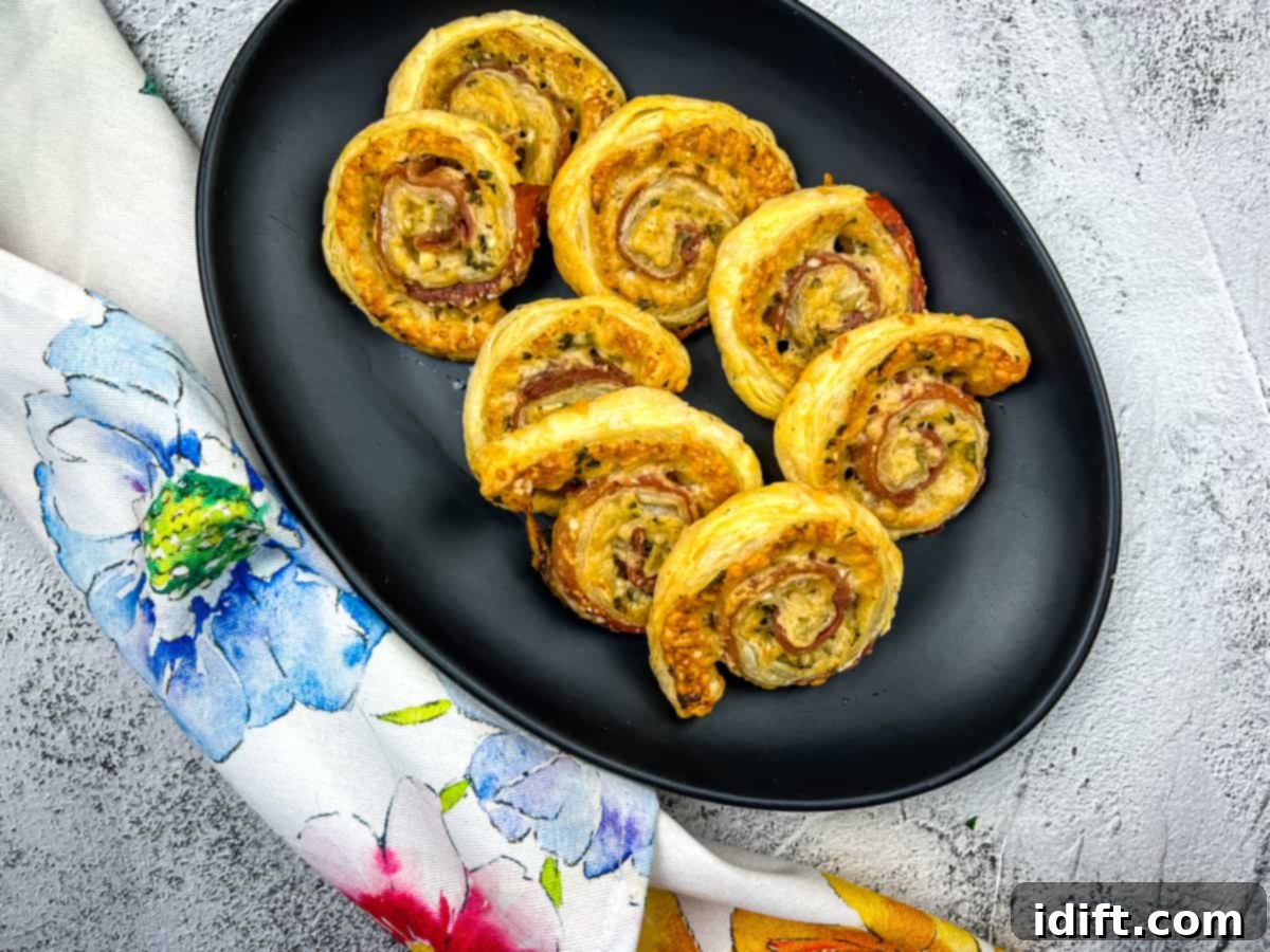 A plate of golden-brown Prosciutto Puff Pastry Pinwheels, artfully arranged and ready to serve.