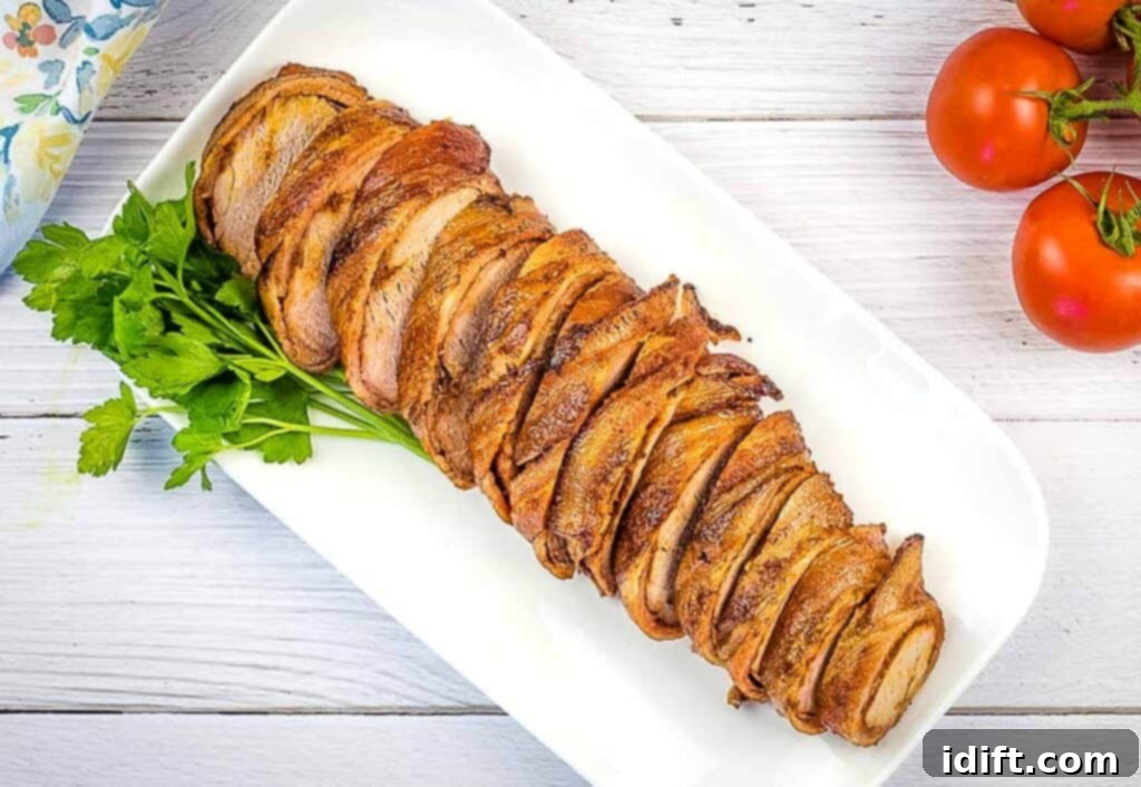 Beautifully sliced bacon-wrapped pork tenderloin served on a elegant white platter, ready for dining.