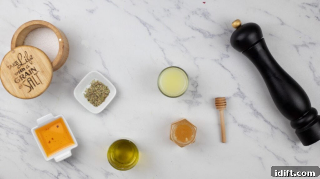 A small collection of dressing ingredients, including a bottle of olive oil, a jar of honey, and other herbs, carefully arranged on a light marble tabletop.