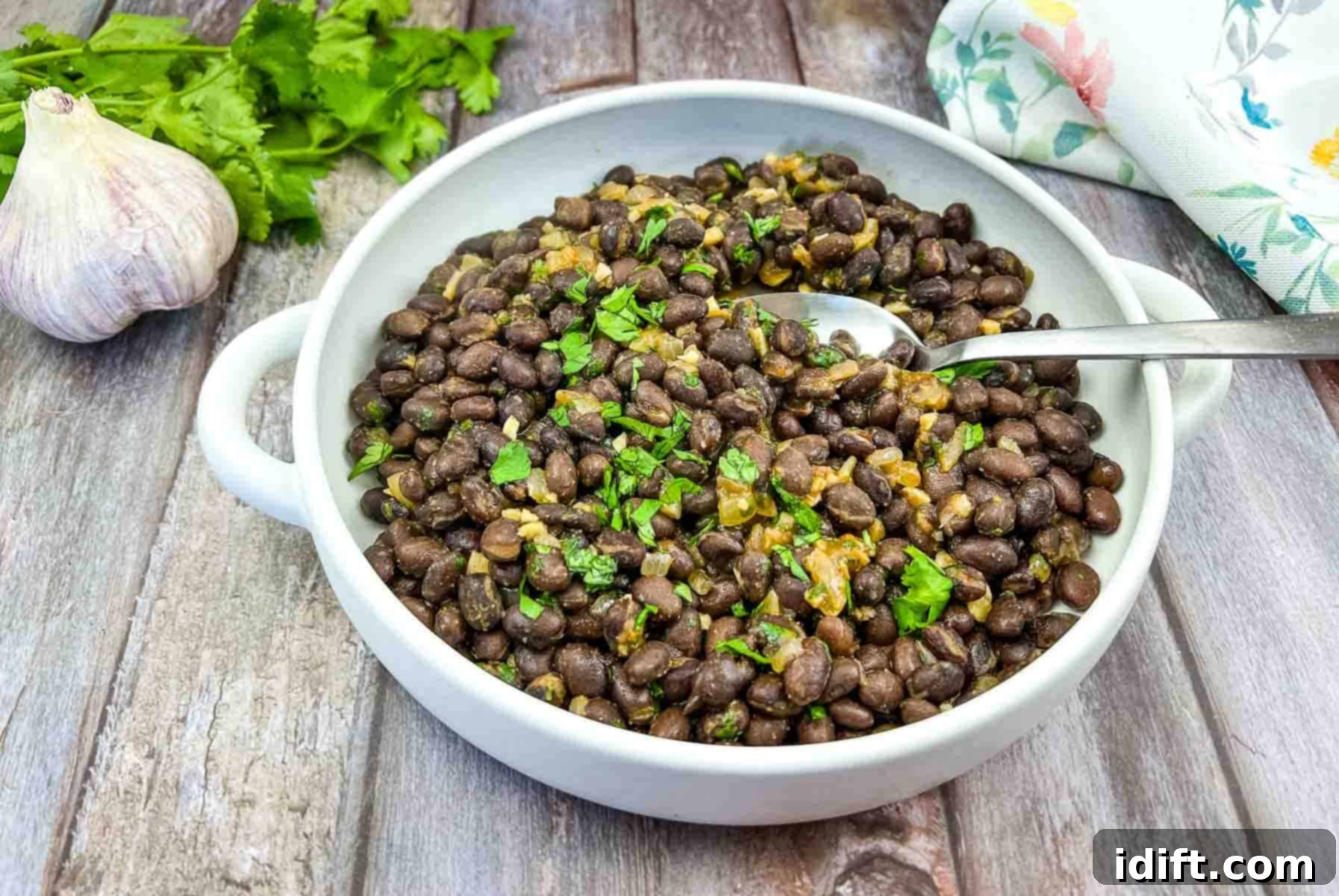 Mexican black beans in a white bowl, garnished with fresh parsley and a slice of garlic.