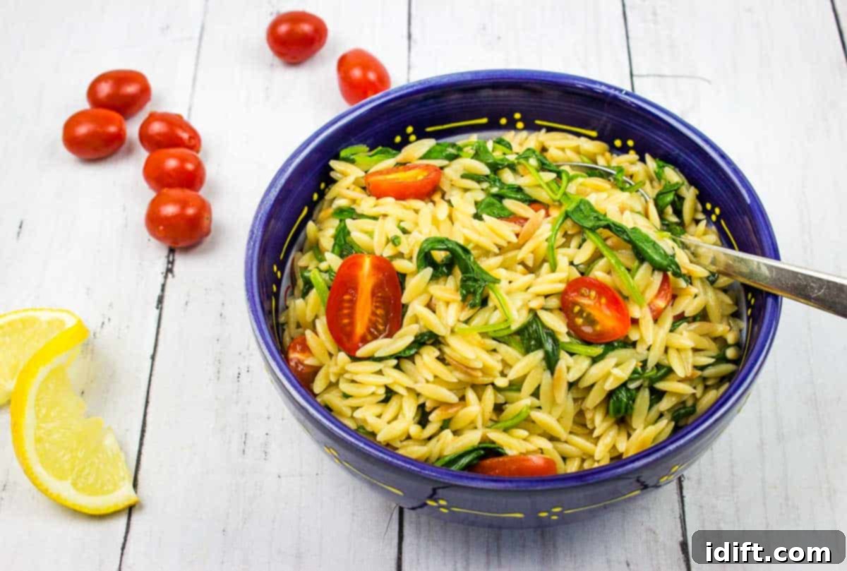 Creamy spinach orzo in a blue bowl with cherry tomatoes nearby and a fork.