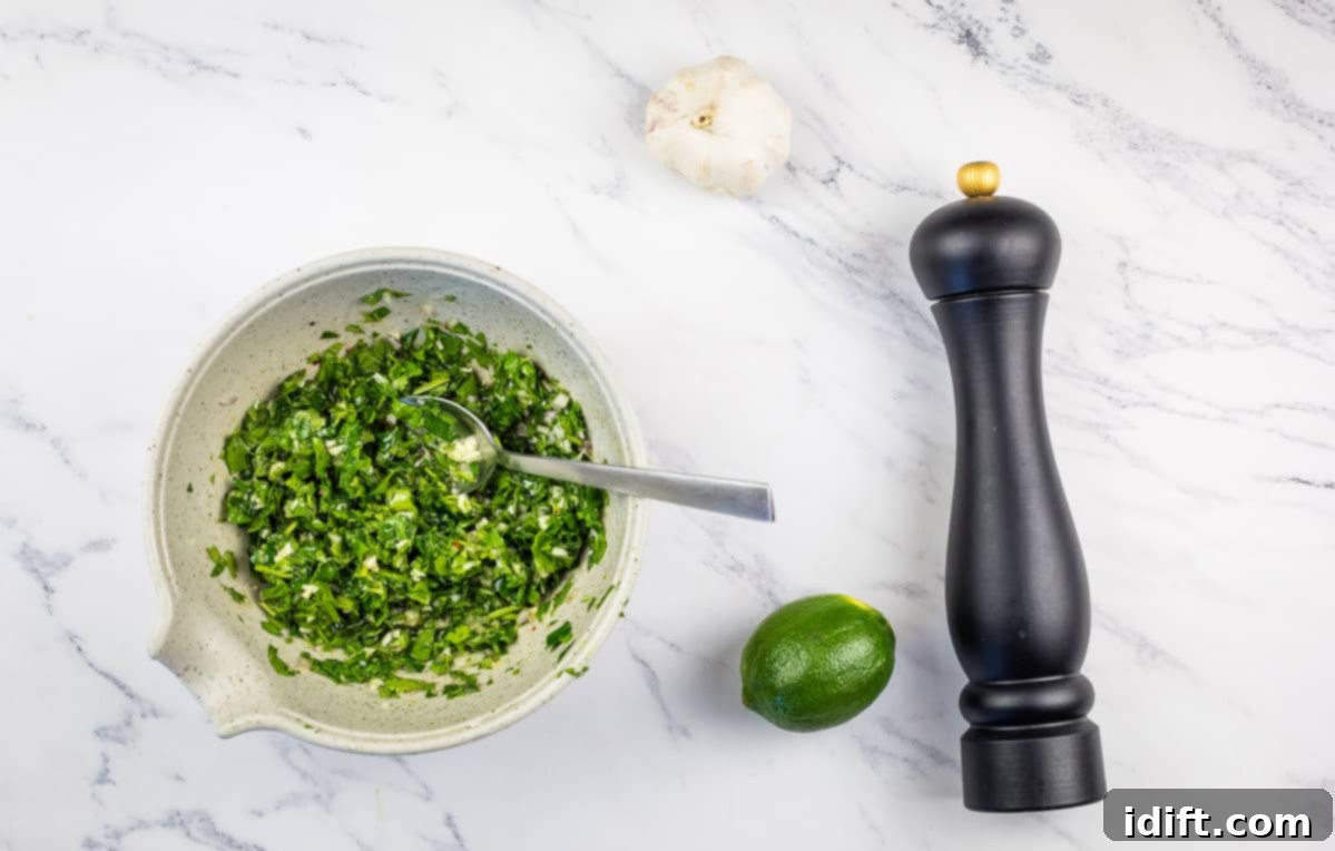 Perfectly sliced Grilled Hanger Steak generously topped with vibrant green Chimichurri Sauce, served on a white plate.