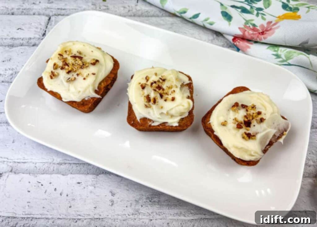 A trio of beautifully presented mini hummingbird cakes, each adorned with creamy frosting and a delicate garnish, on a pristine white plate.