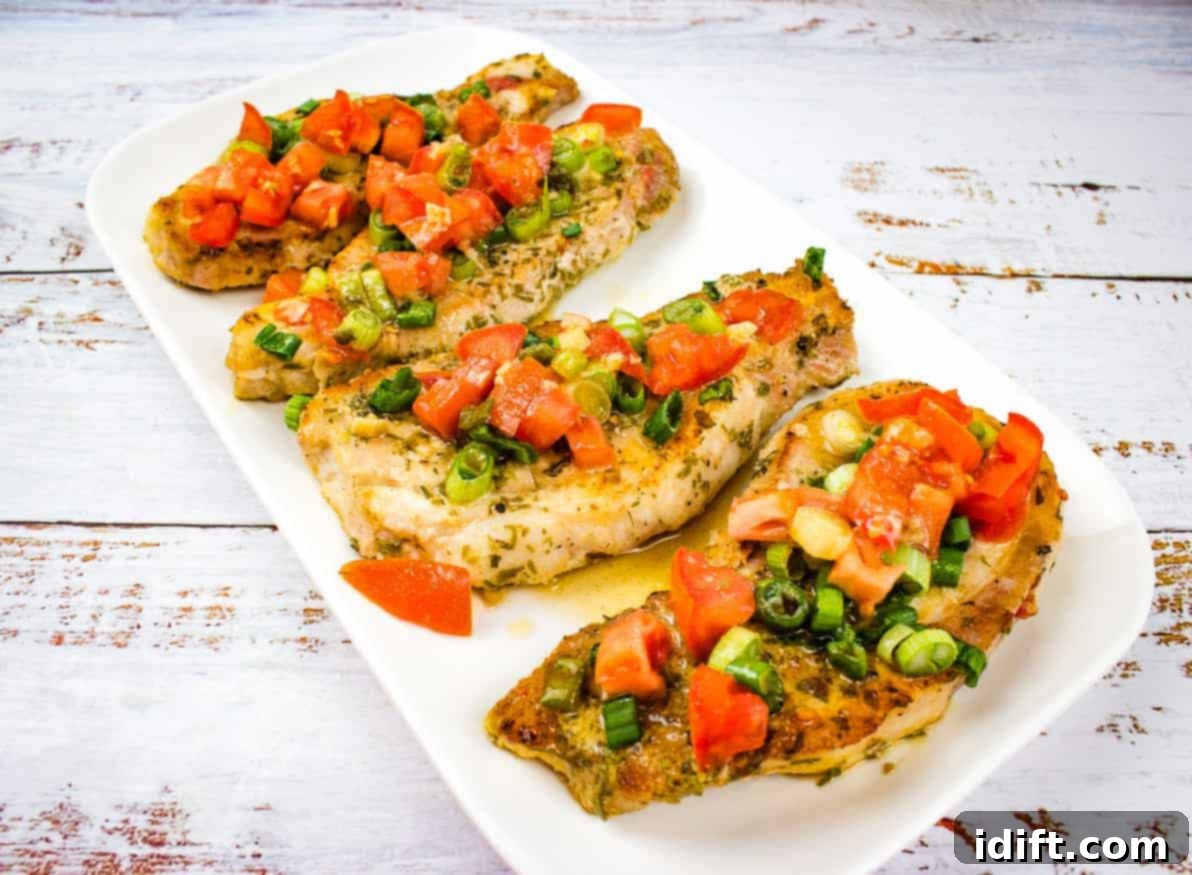 Three perfectly grilled pork chops topped with fresh tomato and green onion relish, served on a white plate.
