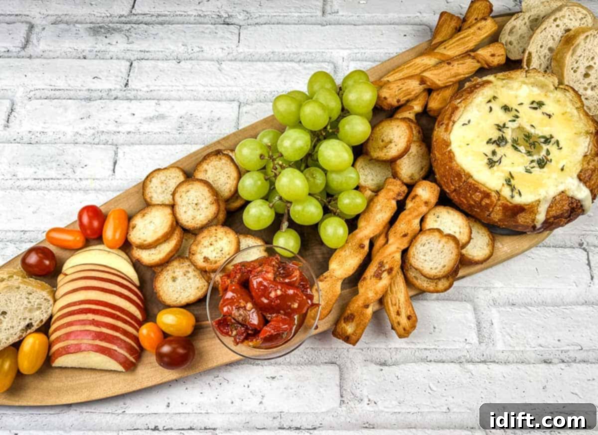 A wooden platter with baked brie in a bowl, cheese, crackers, grapes and bread.