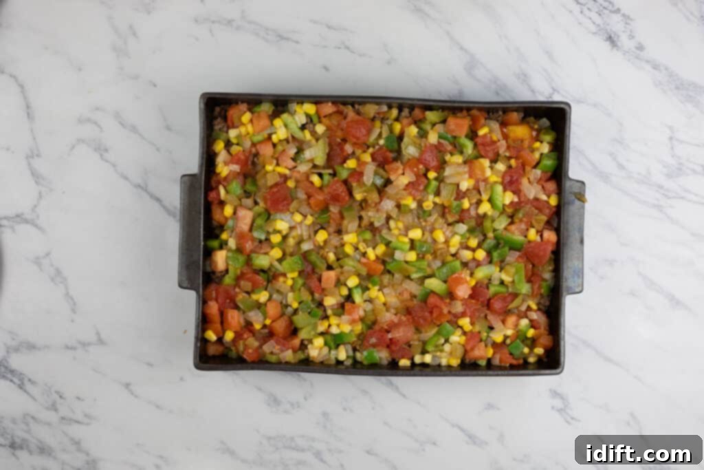 The vibrant vegetable mixture spread over the beef layer in the casserole dish.