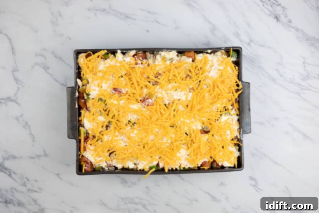 The casserole dish topped with extra shredded cheddar cheese, ready for baking.