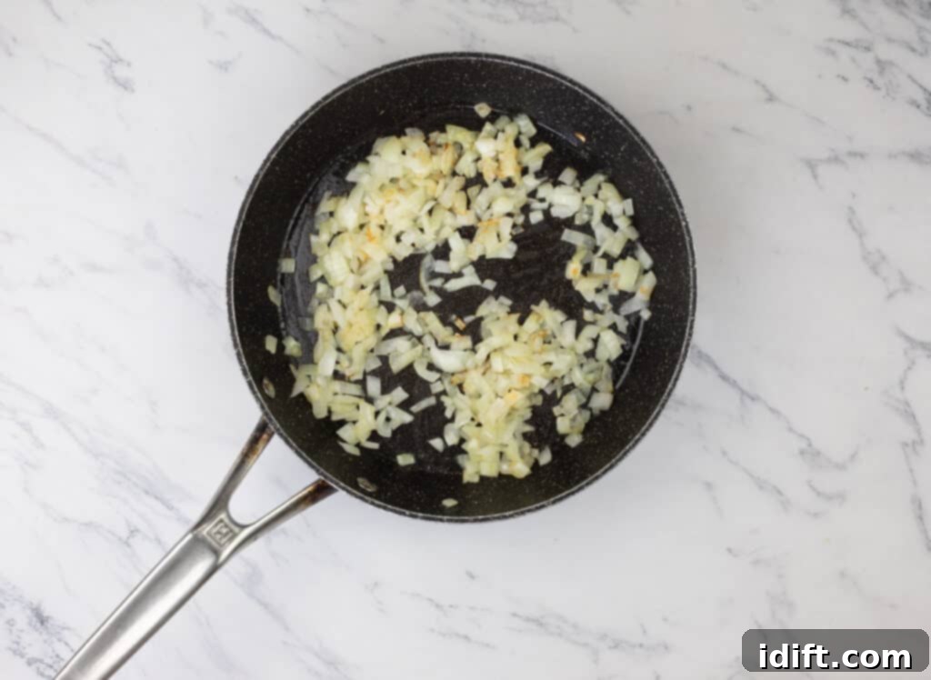 Diced onions being sautéed in a frying pan until soft and fragrant.