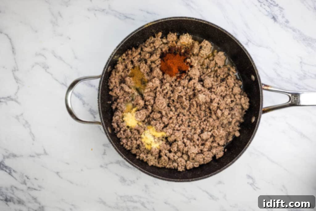Ground beef browning in a frying pan with onions, prior to seasoning.
