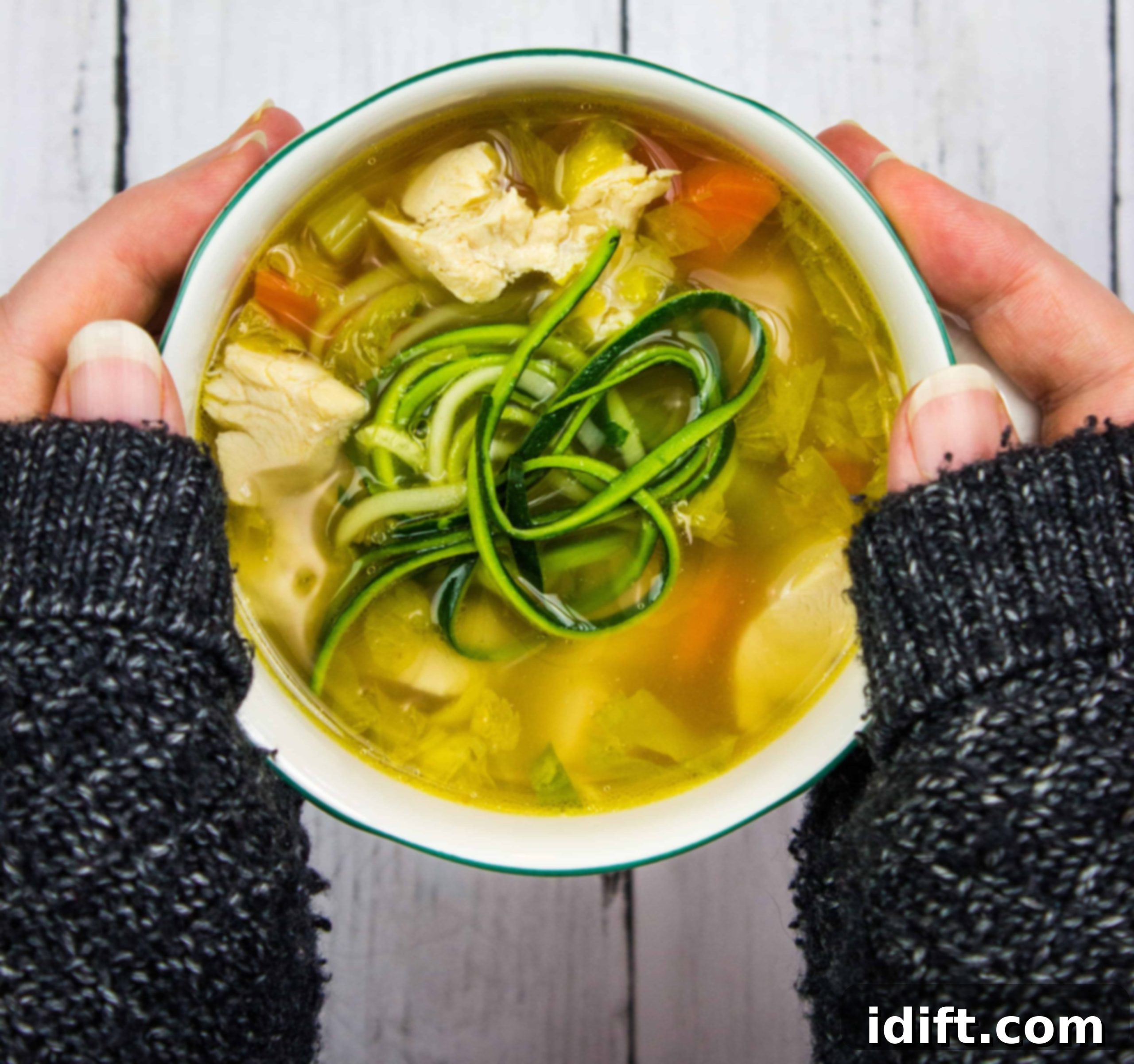 A person holding a bowl of chicken and zucchini soup.