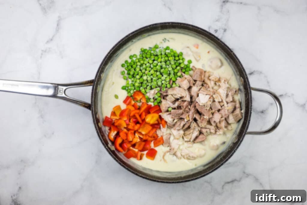 A pan with meat, vegetables and peas in it.