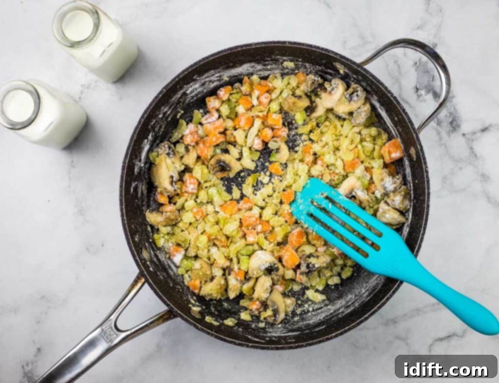 A frying pan with vegetables and a blue spatula.