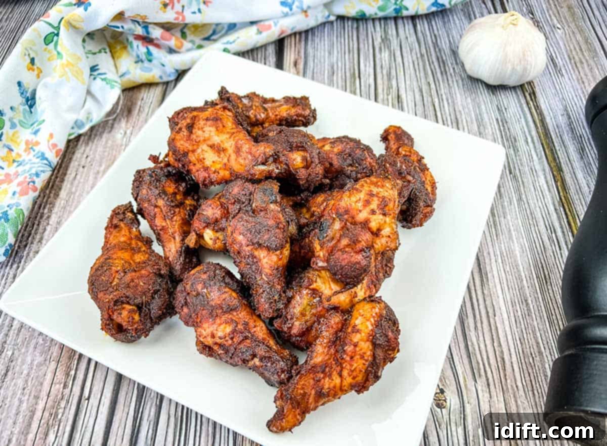 Smoked dry rubbed chicken wings on a white plate with garlic.