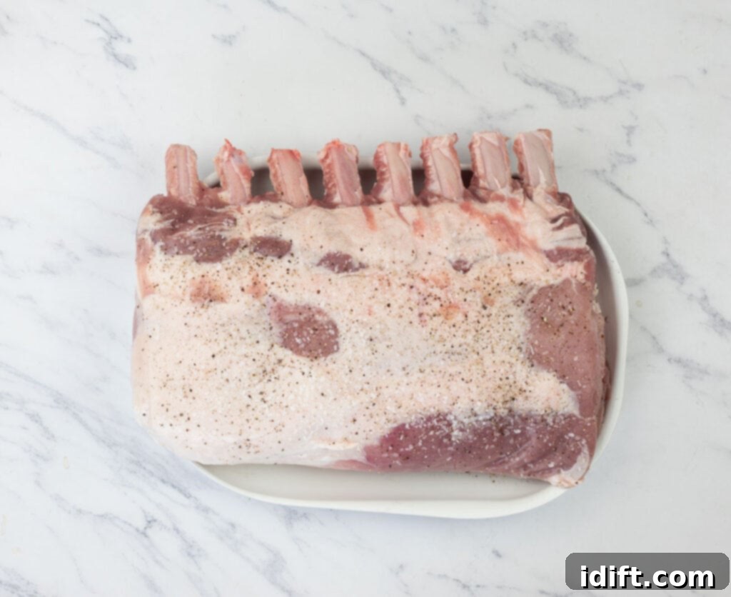 A close-up of a large piece of pork roast generously seasoned with salt and freshly ground black pepper on a cutting board, illustrating the preparation step.