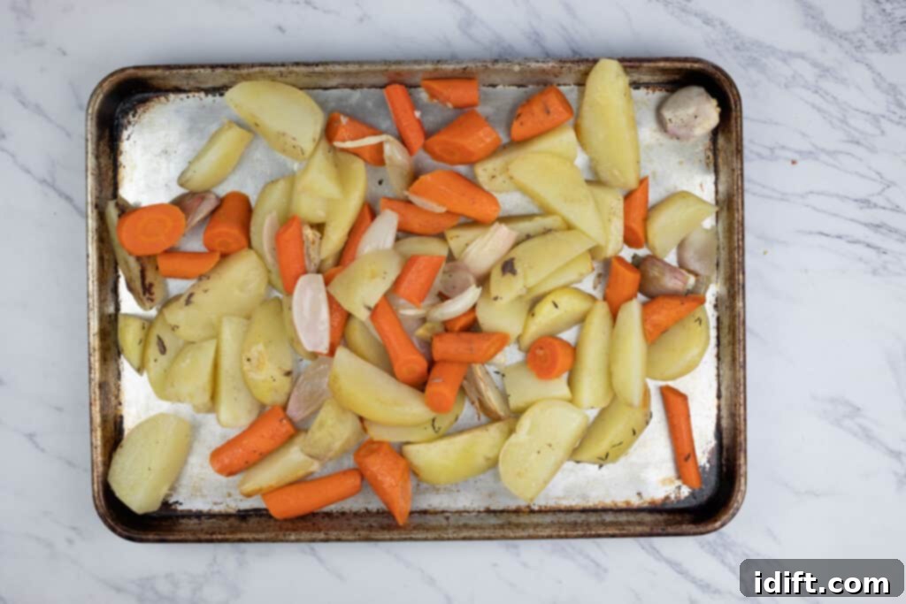 A baking sheet laden with roasted carrots and potatoes, perfectly browned and caramelized, fresh from the broiler.
