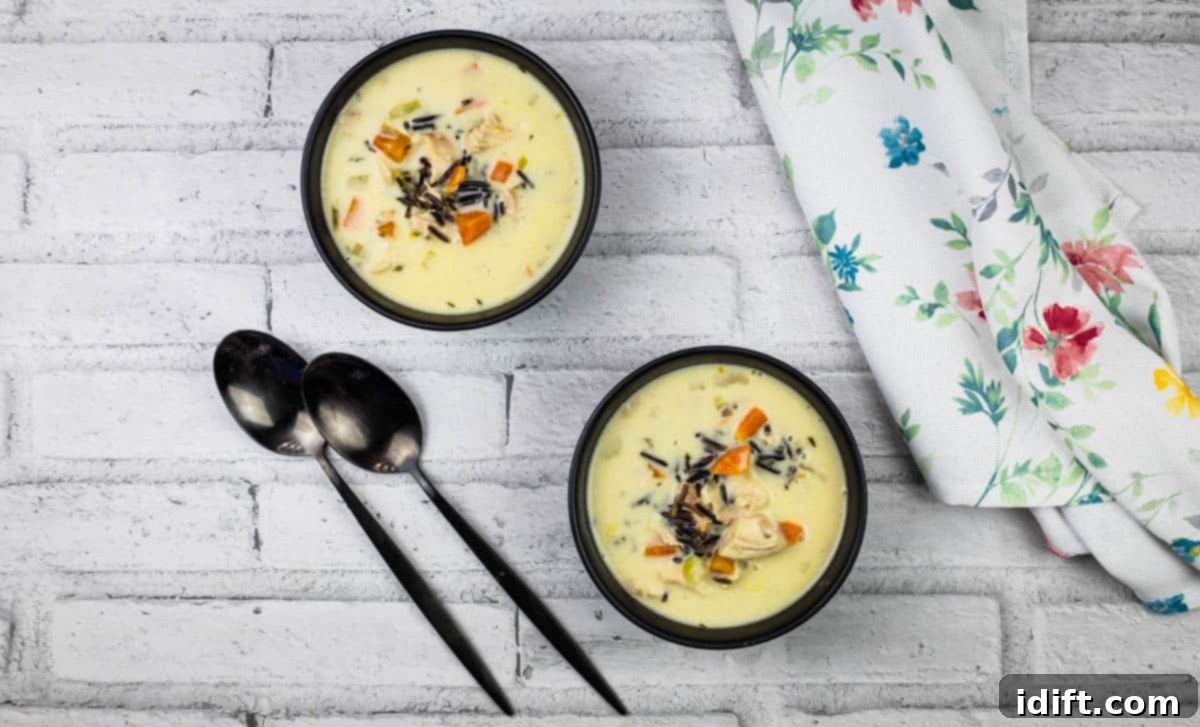 Two bowls of creamy chicken & wild rice soup on a wooden table.