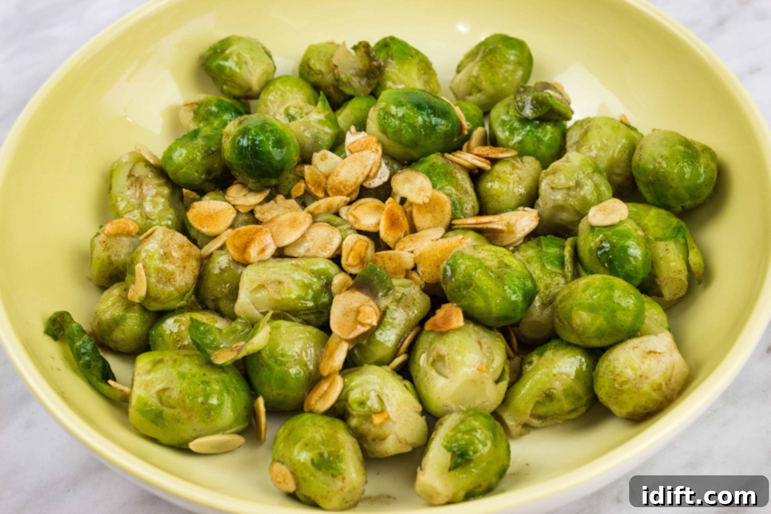 Brussels Sprouts with Brown Butter & Almonds in a shallow yellow bowl, garnished with fresh herbs.