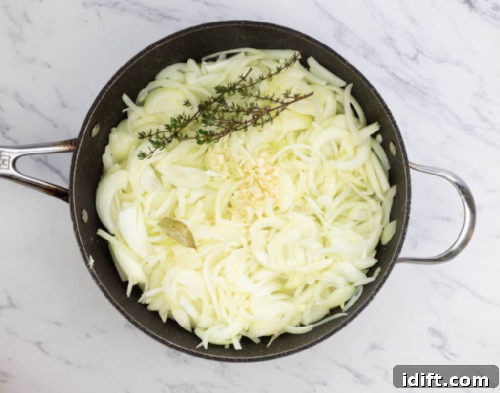 Chef Jenn's Signature French Onion Soup 6 Onions in a pan with a sprig of thyme, beginning the caramelization process.