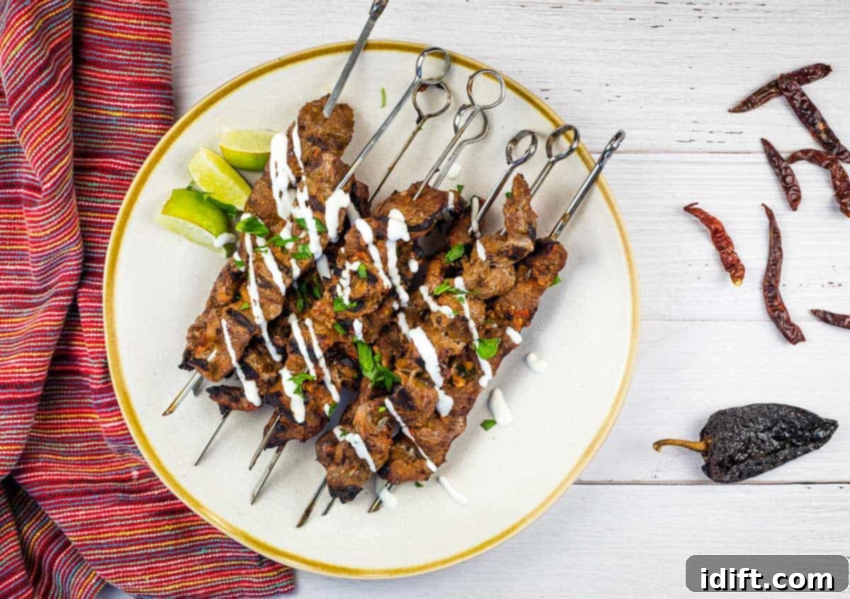 Grilled Steak skewers on a white plate with chilis nearby.