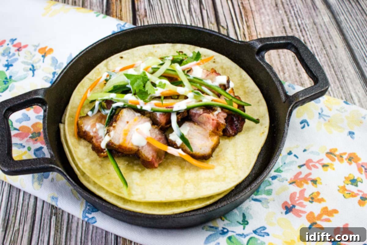 A closeup shot of two tacos filled with smoked pork belly and vegetables.