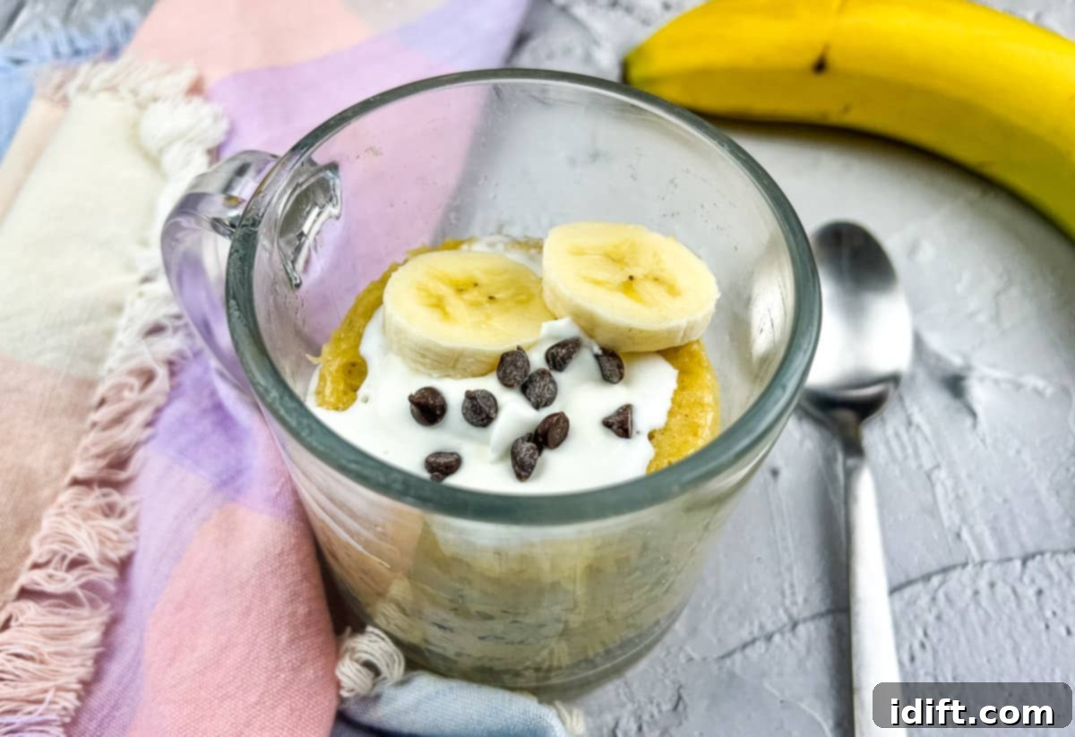 21 Quick & Easy Sweet Treats 8 A banana chocolate chip mug cake in a mug, served with a spoon and fresh banana slices, ready to be enjoyed.