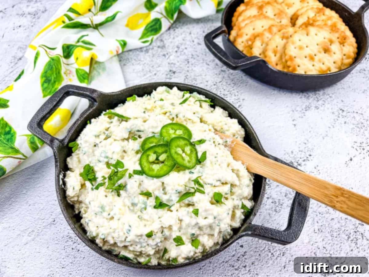 A black bowl overflowing with creamy Artichoke-Jalapeno Dip, accompanied by crispy crackers for dipping.