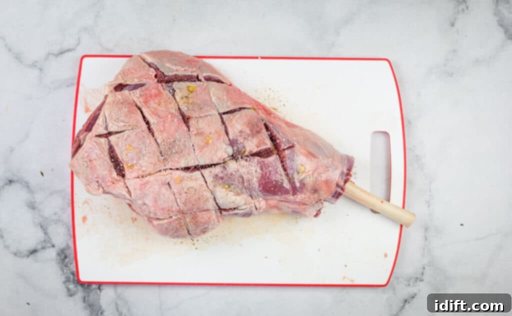 A leg of lamb with its fat cap expertly scored in a cross-hatch pattern and seasoned generously with salt and pepper.