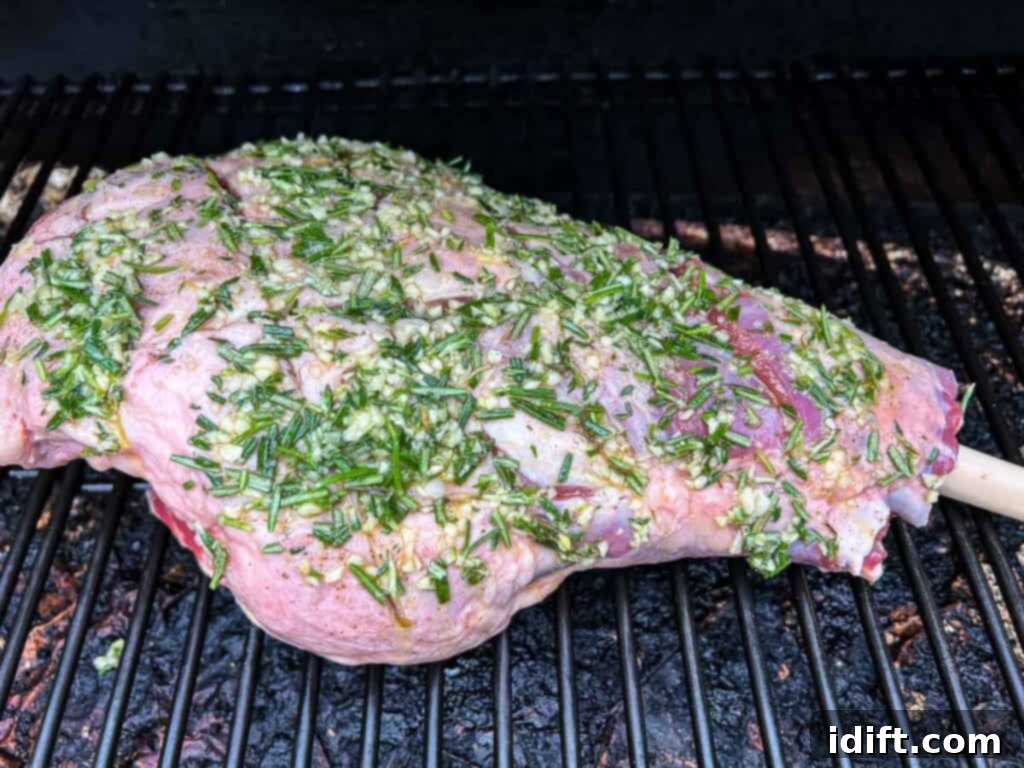 The seasoned leg of lamb gently smoking on the grates of a Traeger pellet grill, absorbing maximum flavor.