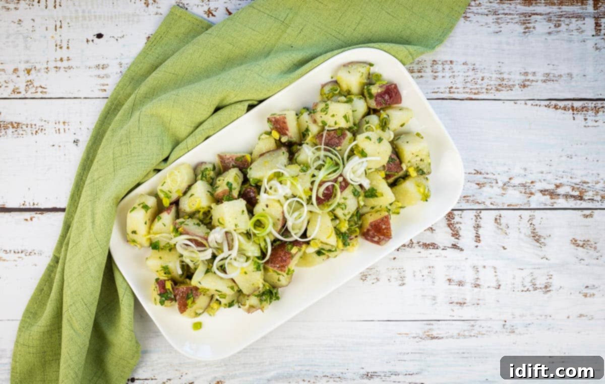 A vibrant potato salad with fresh green herbs and green garlic, served beautifully on a white platter, perfect for a fresh side dish.