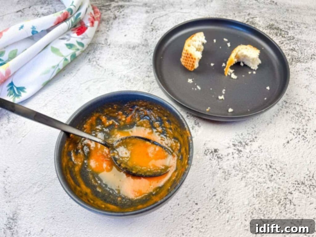 An empty black soup bowl on a rustic wooden table, with a piece of bread on the side.