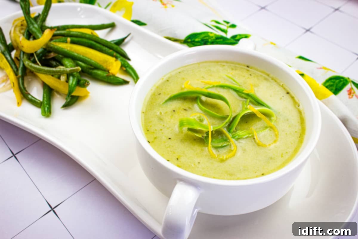 A elegant white bowl filled with vibrant green Cream of Asparagus Soup, garnished with a swirl of cream.