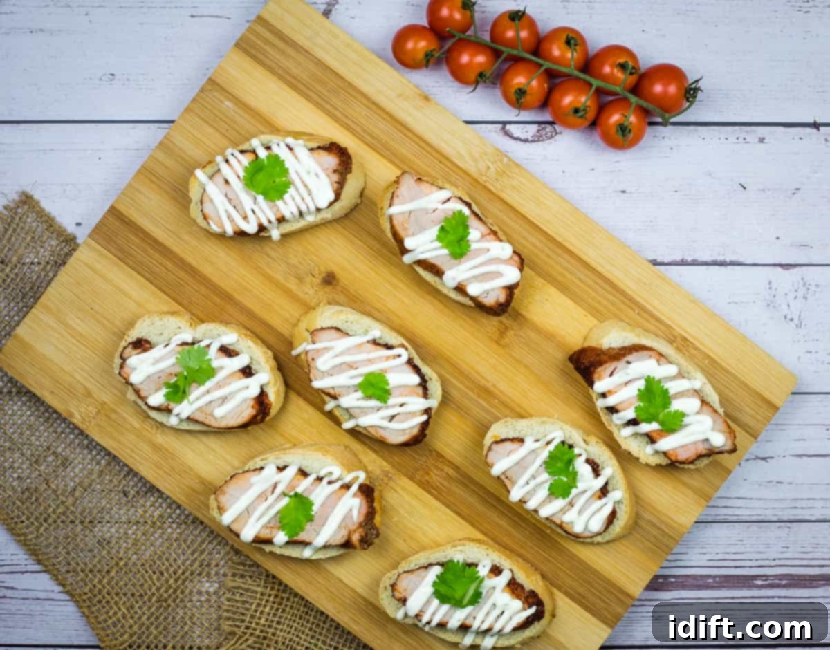 A wooden cutting board beautifully arranged with slices of tender pork tenderloin on crostini, drizzled with a vibrant lime crema.