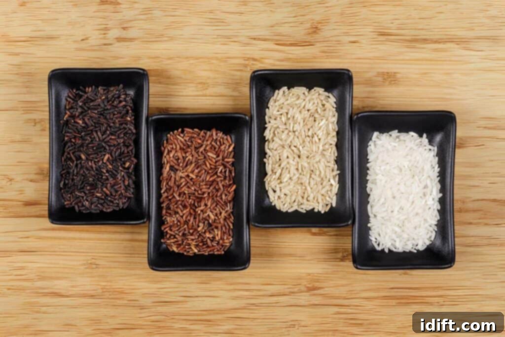 Four distinct varieties of uncooked rice—white, brown, black, and red—elegantly presented in separate black bowls on a rustic wooden surface.