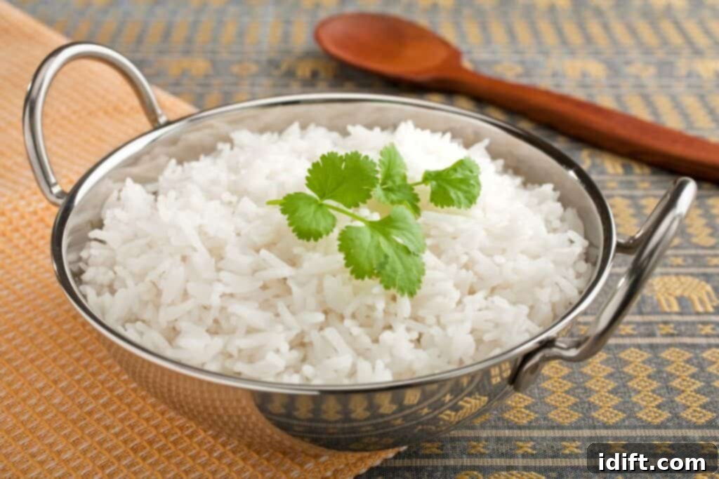 A perfectly cooked bowl of fluffy white rice, delicately garnished with a fresh cilantro leaf, accompanied by a small wooden serving spoon.