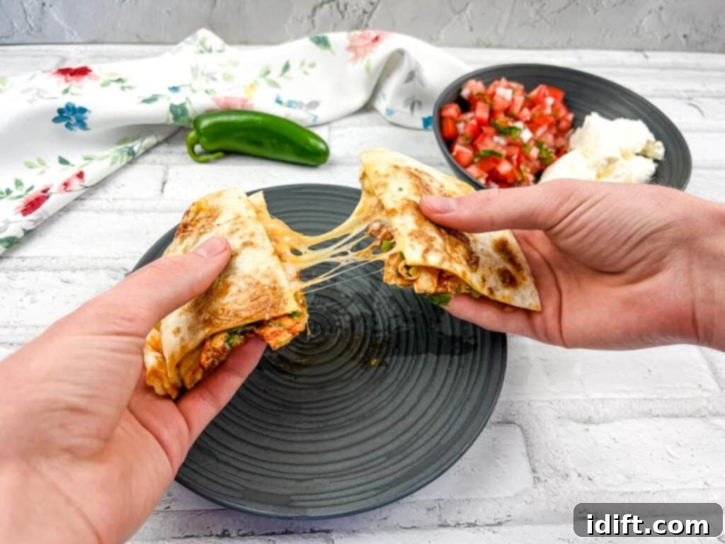 A horizontal shot of two hands pulling the quesadilla apart with gooey cheese in the middle.