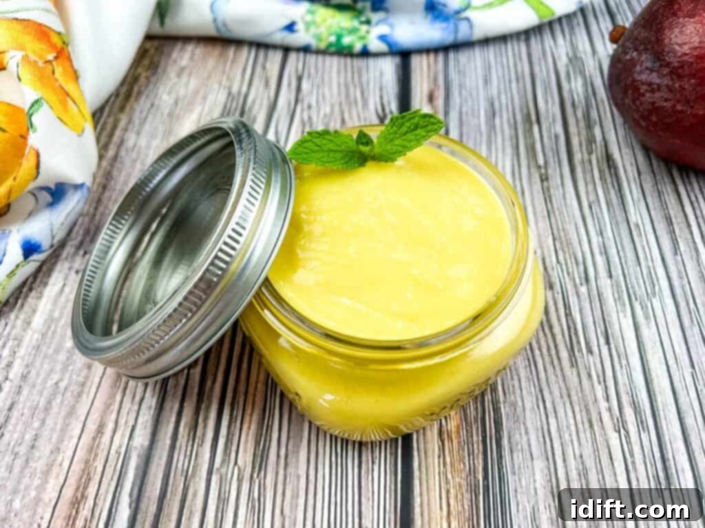 A jar of lemon curd next to an apple and a mint leaf.