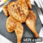 Roasted chicken with seasoning displayed on a slate board with cutlery on the side.