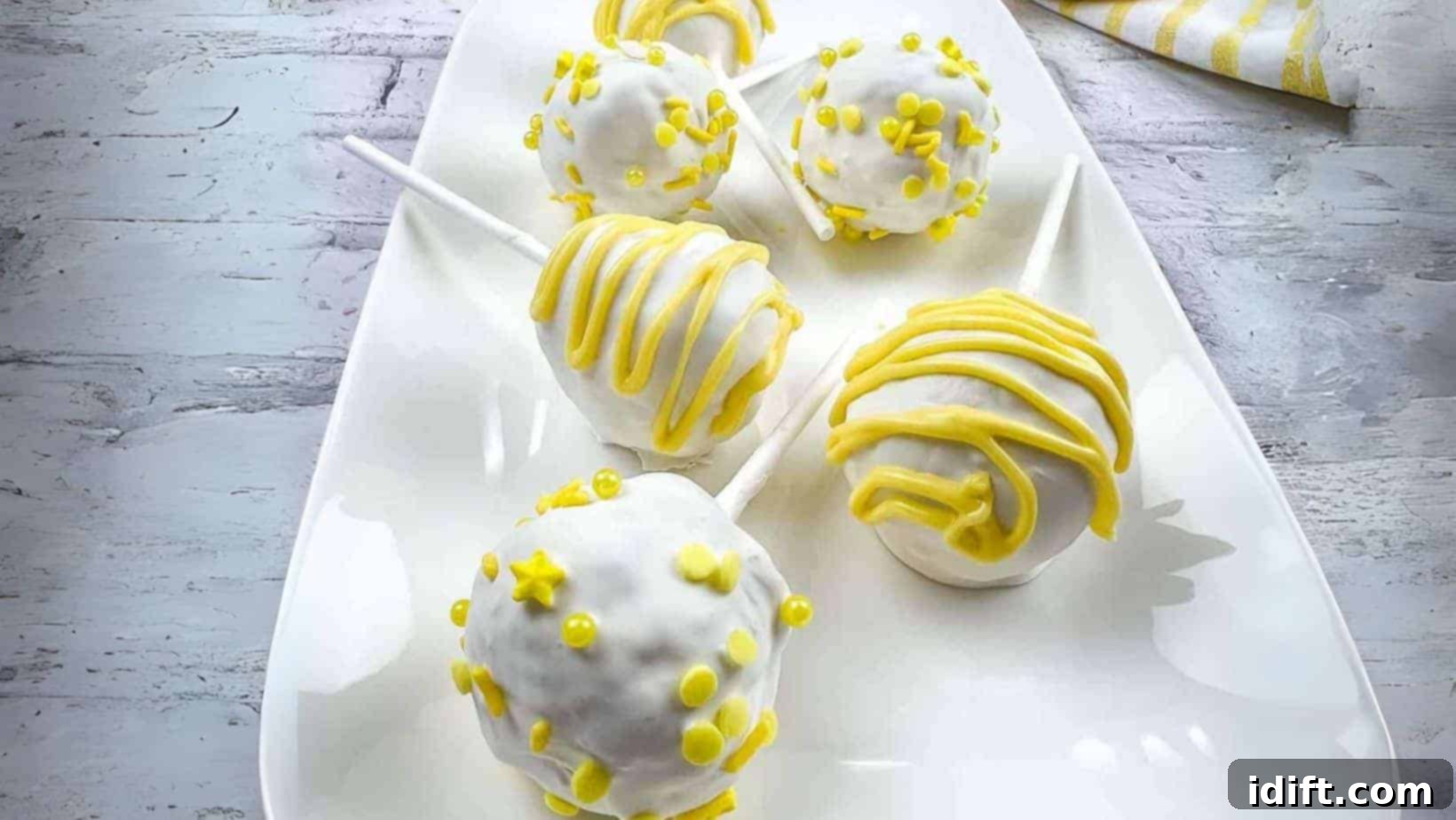 Zesty lemon cake pops on a pristine white plate, garnished with subtle green specks.