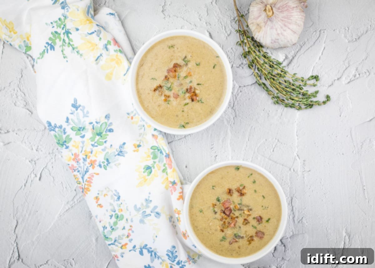 Two steaming bowls of creamy Caramelized Onion & Mushroom Soup, garnished with fresh garlic and thyme.