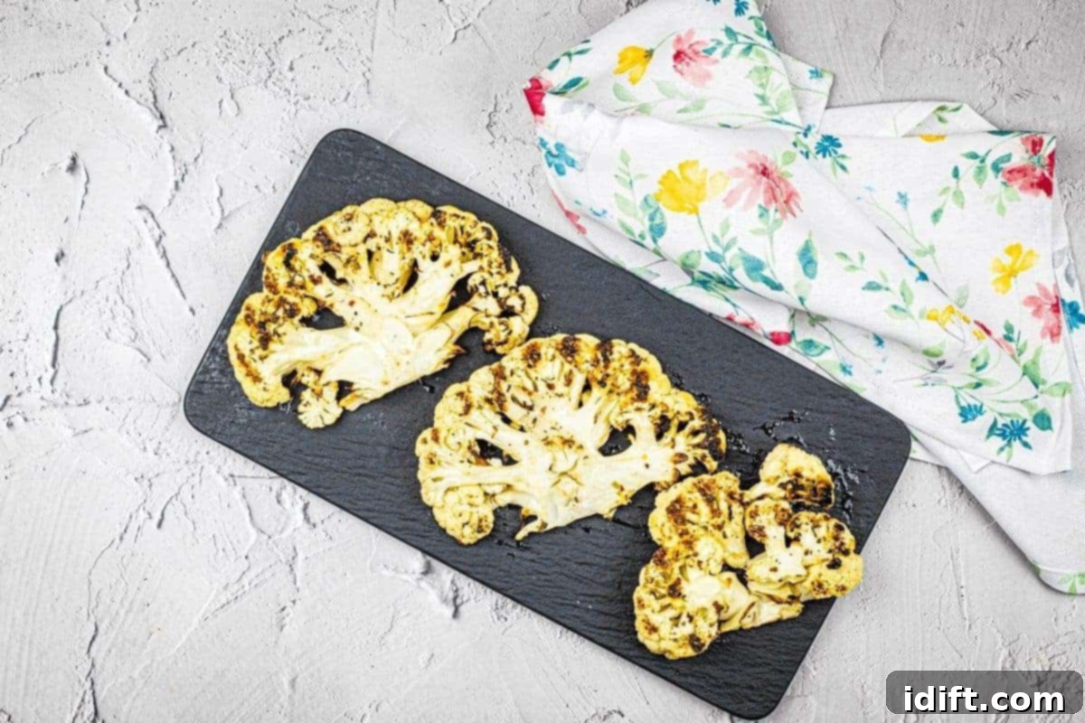 11 Surprising Foods You Have to Try on the Grill 2 Three pieces of grilled cauliflower steaks on a black plate.